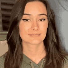 a close up of a woman 's face wearing a green sweater and making a funny face .