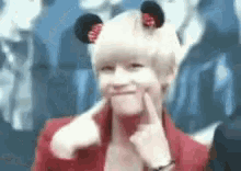 a person wearing a red jacket and a mickey mouse hat is making a funny face .