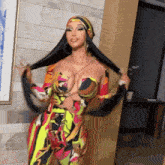 a woman in a colorful jumpsuit with a scarf around her head holds her hair