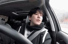 a man wearing a scarf is sitting in a car with a seat belt around his neck