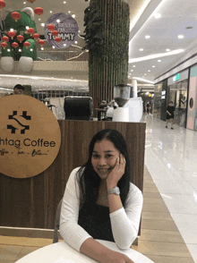 a woman sits at a table in front of a sign that says hig coffee