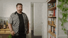 a man in a black and white checkered shirt is standing in front of a bookshelf with the word frie written on it