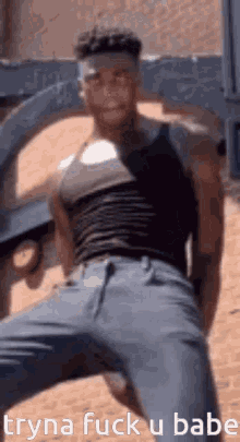 a man in a black tank top and blue jeans is standing in front of a wall .