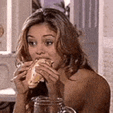 a woman is sitting at a table eating a sandwich and drinking a glass of water .