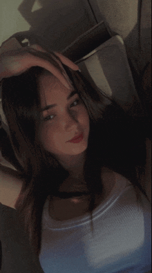 a woman in a white tank top holds her hand to her forehead