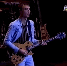 a man in a blue shirt is playing a guitar in a dark room