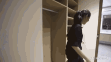 a woman is walking through a closet in a room with a mirror .