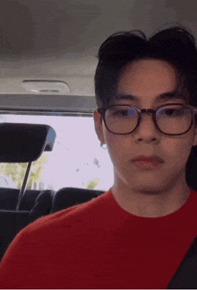 a young man wearing glasses and a red shirt is in a car .