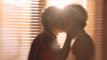 a couple kissing in front of a window with blinds on it