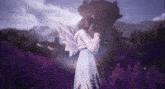 a woman in a white dress with fairy wings stands in a field of purple flowers