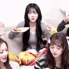 a group of girls are sitting on a couch eating food . one girl is holding a plate of food .