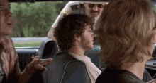a man with curly hair is sitting in the back seat of a car with two other men .