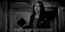 a black and white photo of a woman in a leather jacket standing in a room .