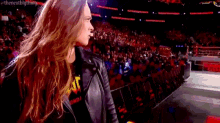 a woman in a leather jacket is standing in front of a crowd of people in a stadium .