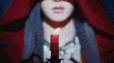 a woman in a red cape is holding a lit candle in front of her face