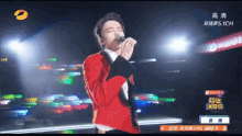 a man in a red jacket is singing into a microphone on a stage