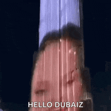 a woman is standing in front of a tall building with the words `` hello dubaiz '' written on it .