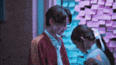 a boy and a girl are looking at each other in front of a wall full of sticky notes
