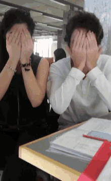 a man and a woman are covering their faces while sitting at a table