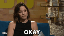 a woman sitting on a couch with the word okay on her chest
