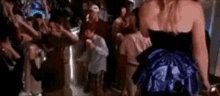 a woman in a blue dress is standing in front of a crowd of people dancing at a party .