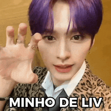 a young man with purple hair and a leopard print jacket is waving his hand .