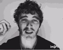 a man with curly hair and a beard is wearing headphones and smiling in a black and white photo .