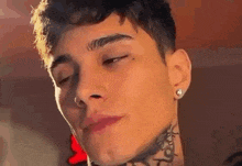 a close up of a young man 's face with a tattoo on his neck and earrings .