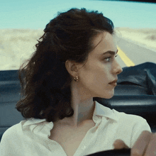 a woman wearing a white shirt and gold hoop earrings is sitting in a car
