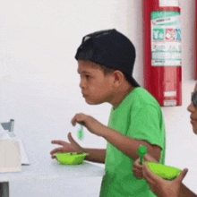 a boy in a green shirt is eating from a bowl