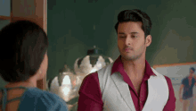 a man in a red shirt and white vest is looking at a woman