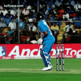 a cricket player is walking towards the wicket while holding a bat .