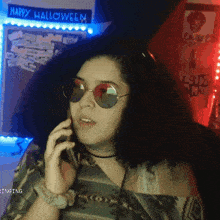 a woman wearing sunglasses talks on a cell phone in front of a happy halloween sign