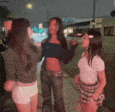 a group of young women are standing on a sidewalk at night .