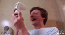 a man is laughing while holding a remote control in his hands .