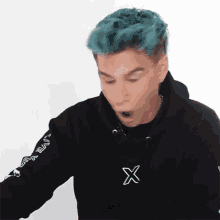 a man with blue hair is wearing a black hoodie with a white x on the sleeve