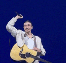 a man is singing into a microphone while holding a guitar in front of a blue background .