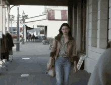 a woman walking down a sidewalk in front of a store that says ' a & a ' on it