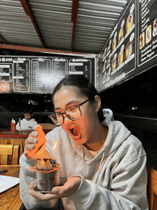 a girl with glasses is holding a candle in front of a menu that says ' sandwich baker '