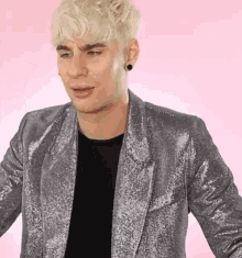 a man with blonde hair is wearing a silver jacket and a black shirt .