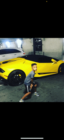 a young boy is standing next to a yellow sports car in a parking garage .