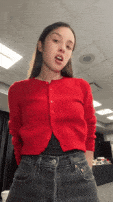 a woman wearing a red cardigan and black jeans is standing in a room