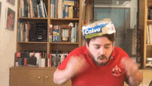 a man wearing a red shirt has a box of calvo on top of his head