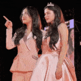 two women are standing next to each other and one is wearing a crown .