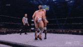 two men are wrestling in a wrestling ring while a referee stands behind them .