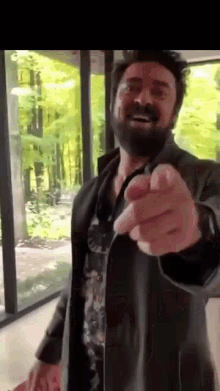 a man with a beard is pointing at the camera while wearing a black jacket .