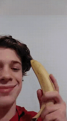a young man in a red shirt is holding a banana in his hand