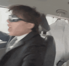 a man in a suit is driving a car and wearing sunglasses
