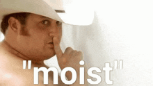 a shirtless man in a cowboy hat is covering his mouth with his finger and the words " moist " behind him