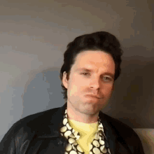 a man wearing a leather jacket and a polka dot shirt is making a face .